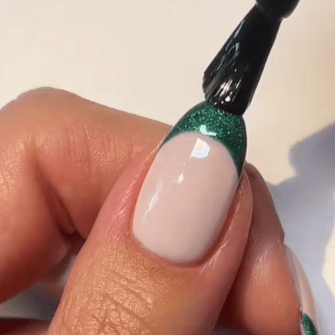 A hand does a French manicure with green glitter varnish on the nail top.