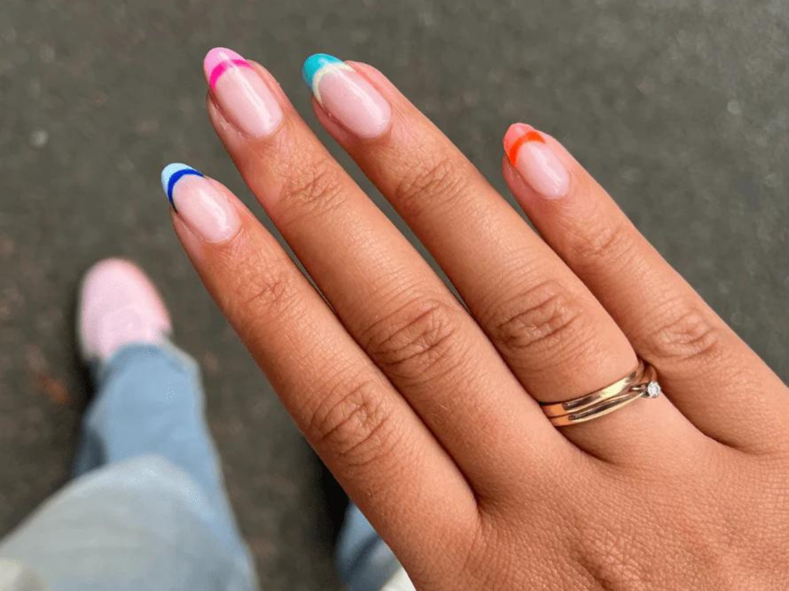Hand with colorful nail polish stripes on the nails and a ring on the ring finger.