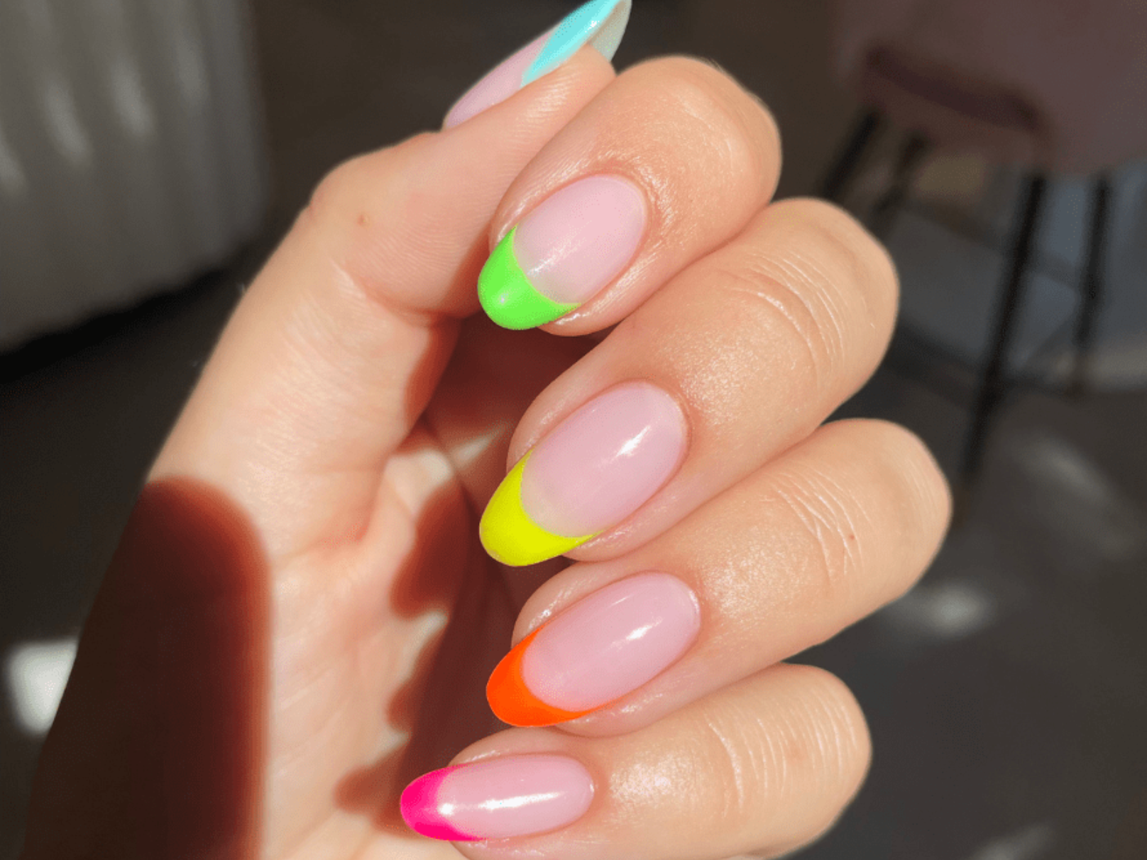 Close-up of a hand with long nails, decorated with a colorful, neon French manicure in pink, orange, yellow, green and blue.