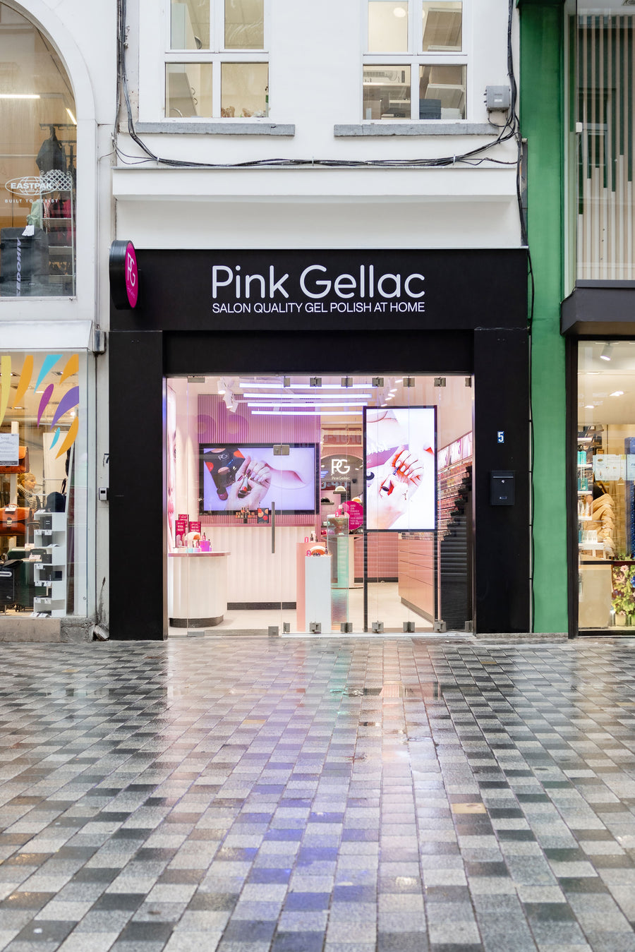 Front view of a shop called "Pink Gellac" with glass doors and pink interior, located on a tiled shopping street.