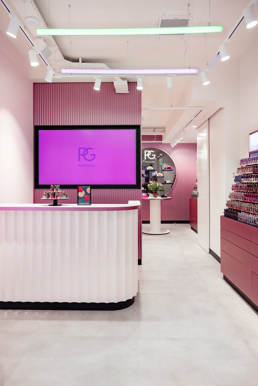 Interior of a modern store with a pink and white color scheme, a counter with a screen above it, and products displayed along the walls.