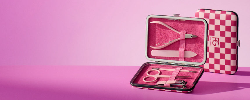 Pink manicure set in an open case with scissors and nail clippers, against a pink background.