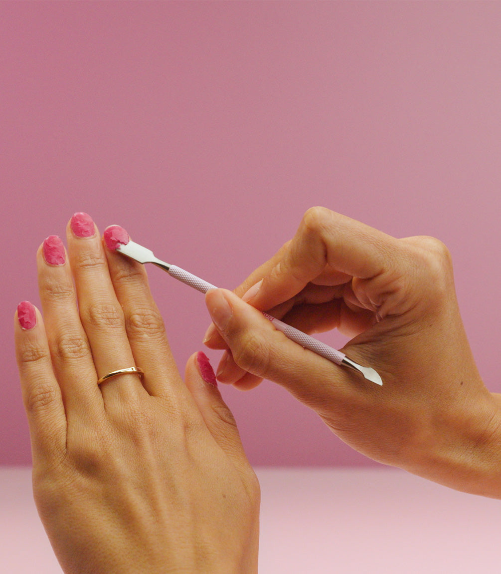 Removing softened gel polish from a nail with a cuticle stick.