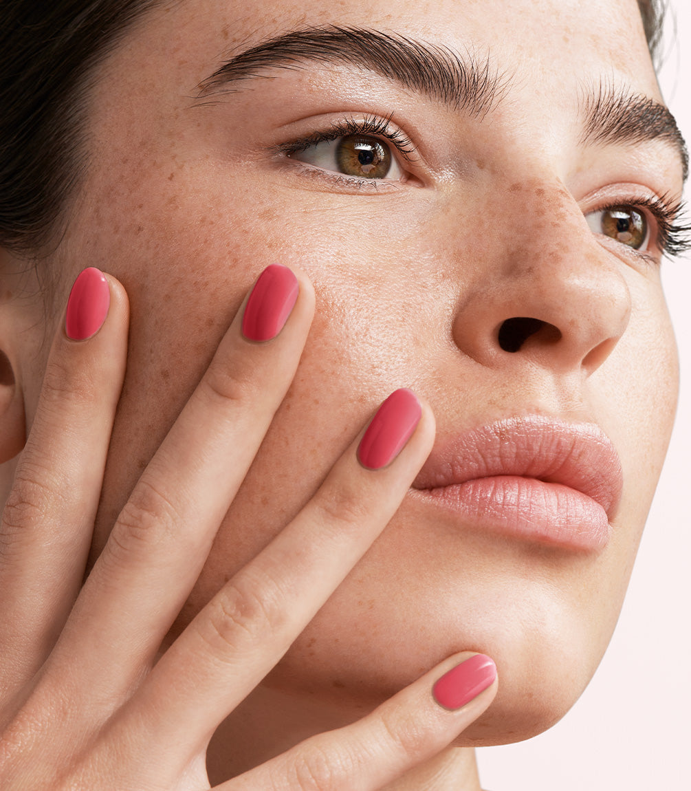 Close-up of a woman with Pink Gellac 142 Coral Red manicured nails near her face.