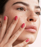 Close-up of a woman with Pink Gellac 142 Coral Red manicured nails near her face.