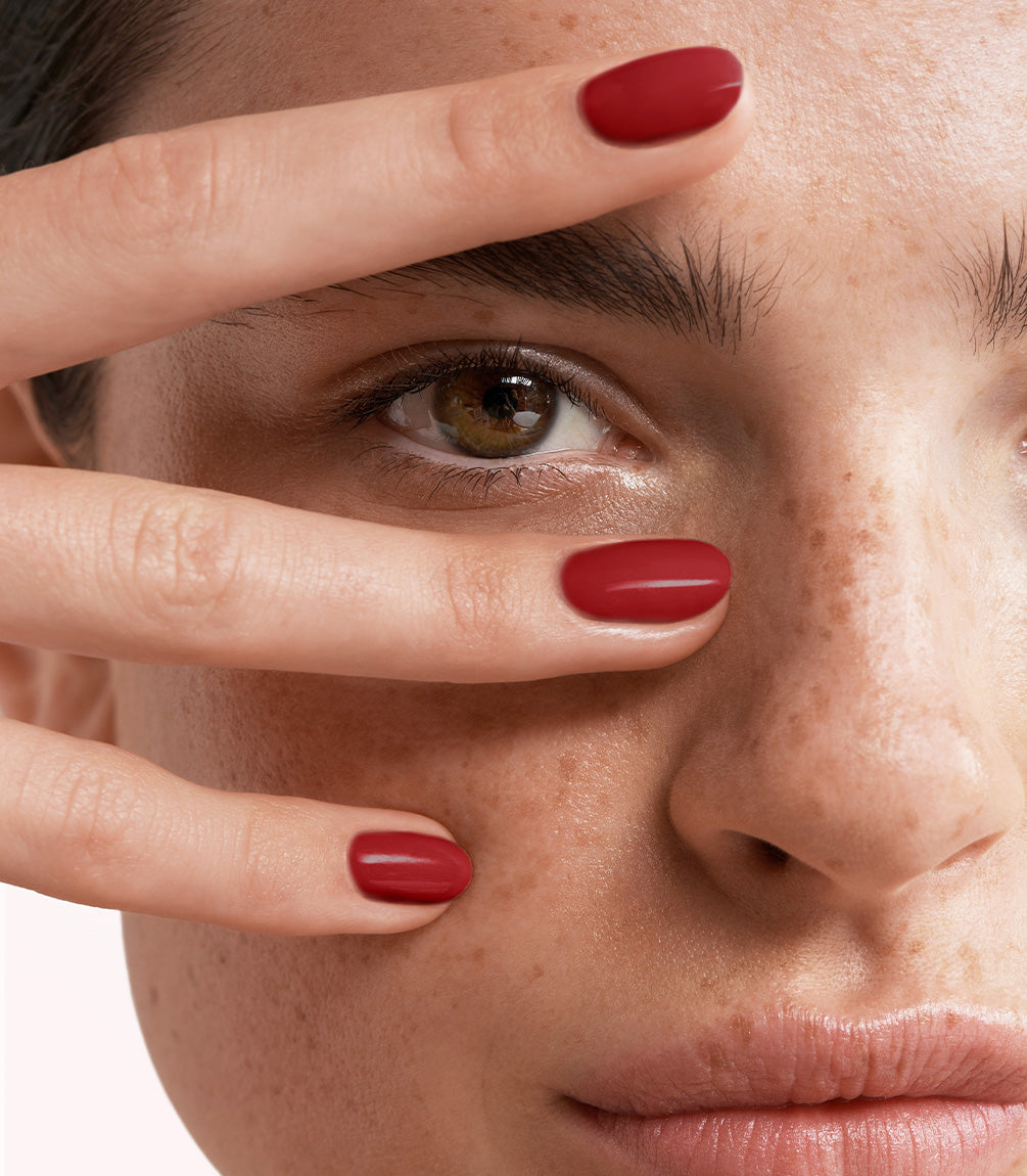 Close-up of a woman with Pink Gellac 235 Ruby Red manicured nails near her face.