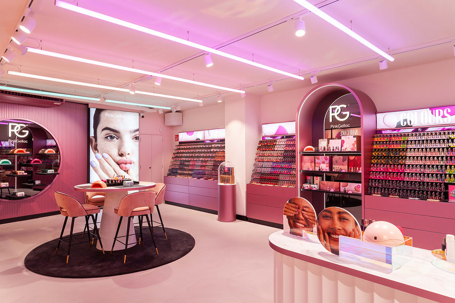Pink and modern decorated nail salon with displays full of nail polishes, a table with pink chairs and colorful decorations.