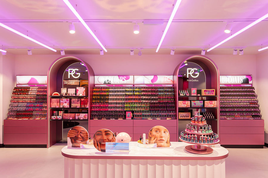 A colorful store design with pink lighting, with racks full of nail polish in various colors and a central table with marketing material and products.