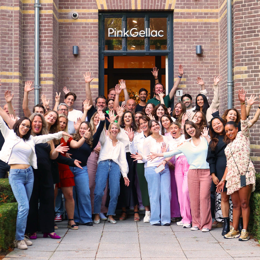 Group of people happily posing in front of the Pink Gellac building, with their hands in the air.