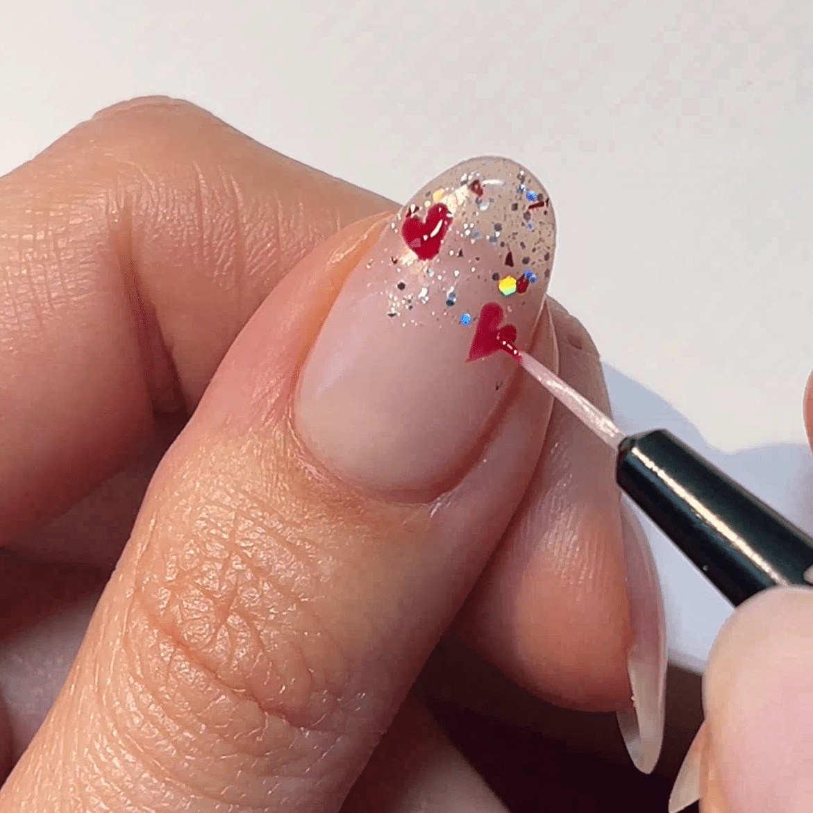 Nail with glitter and red hearts is decorated with a brush.