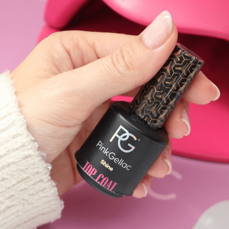 Hand holding a bottle of Pink Gellac Shine Top Coat nail polish with pink background.
