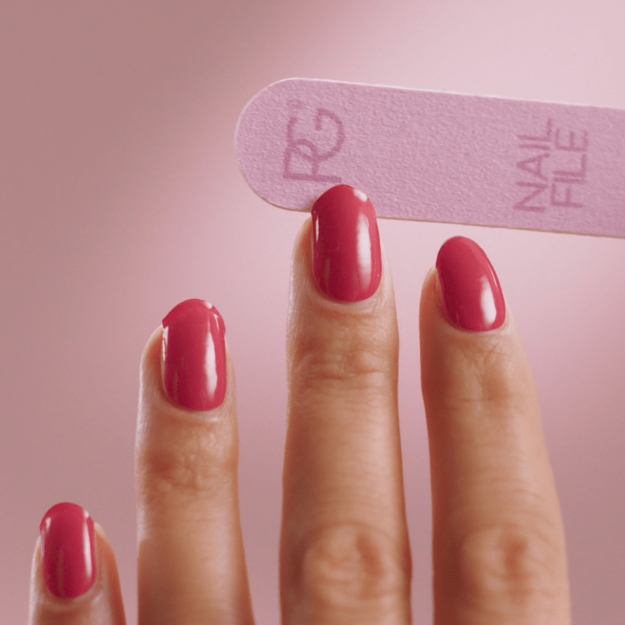 A close-up of hands with pink painted nails, while a pink nail file is used.