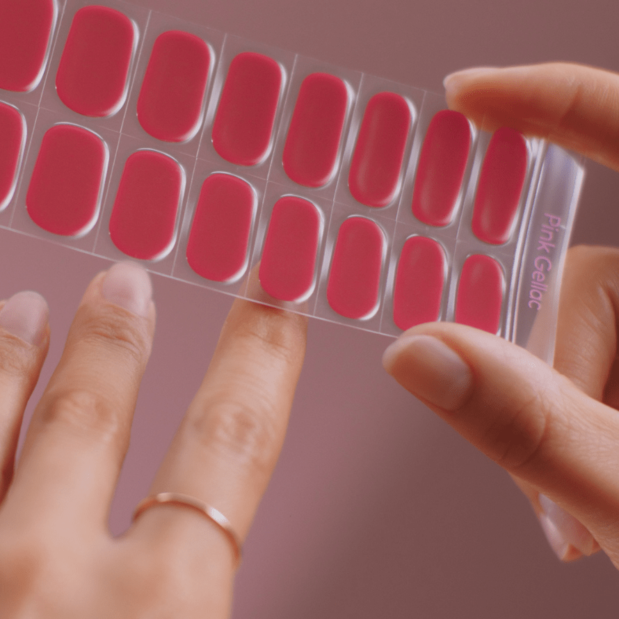 Two hands hold a strip of red nail stickers against a pink background.