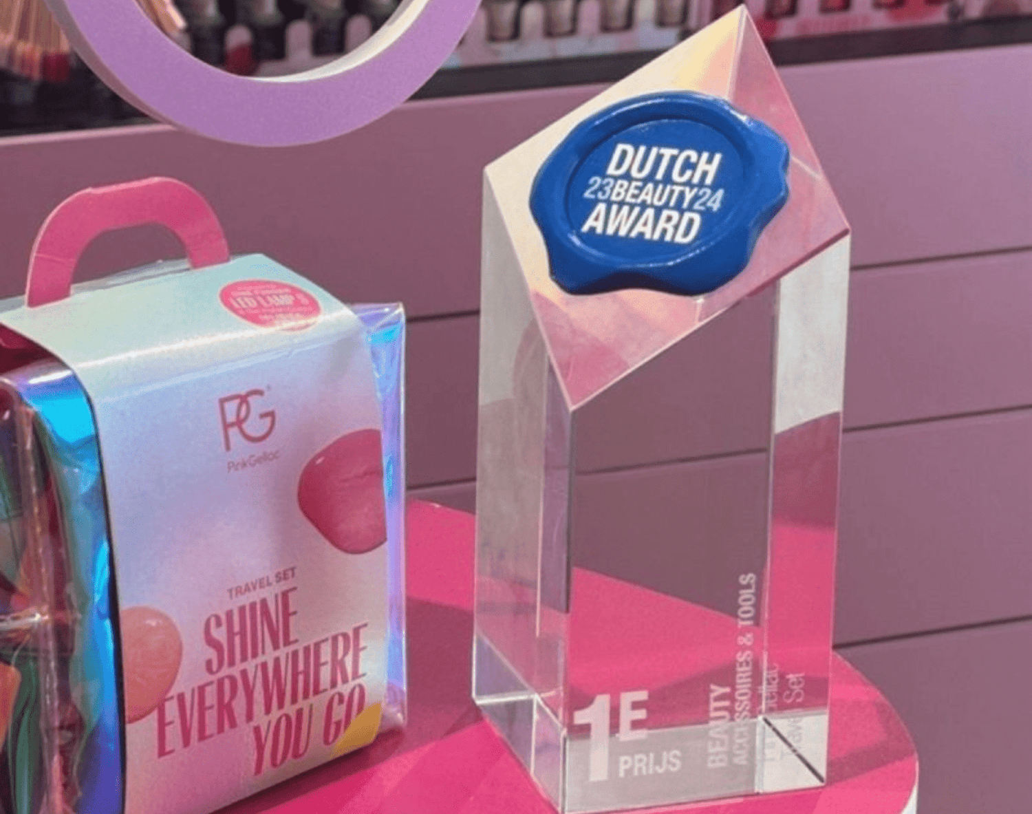 Glittering beauty award and travel set on a table with a pink background full of nail polish bottles.