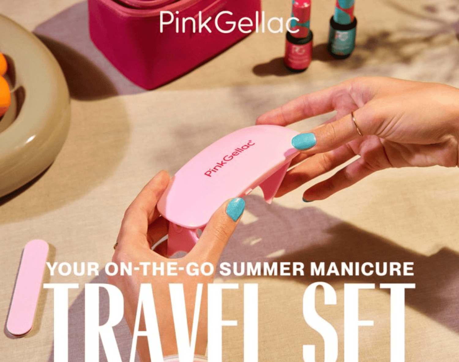 Person with blue painted nails holds a pink Pink Gellac UV lamp, with a pink bag and bottles of nail polish in the background, with the text Your On-The-Go Summer Manicure Travel Set.