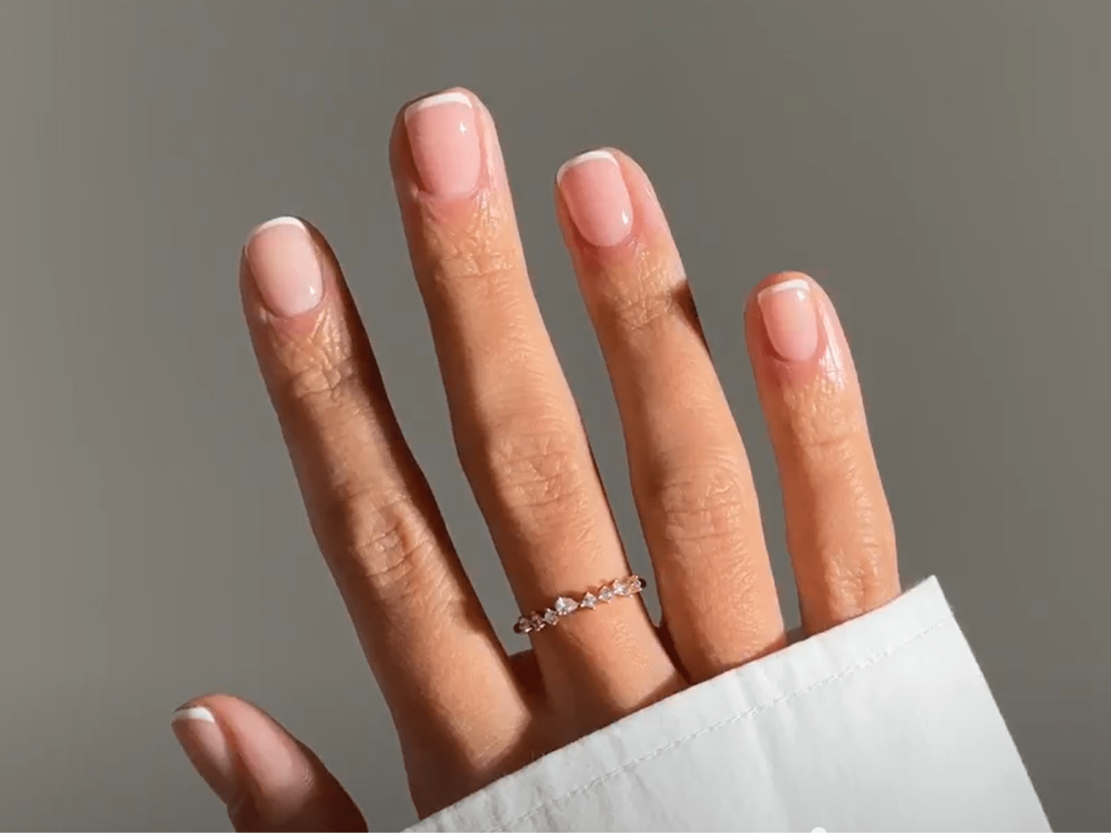 A hand with a ring on the middle finger and cared for with a French manicure.