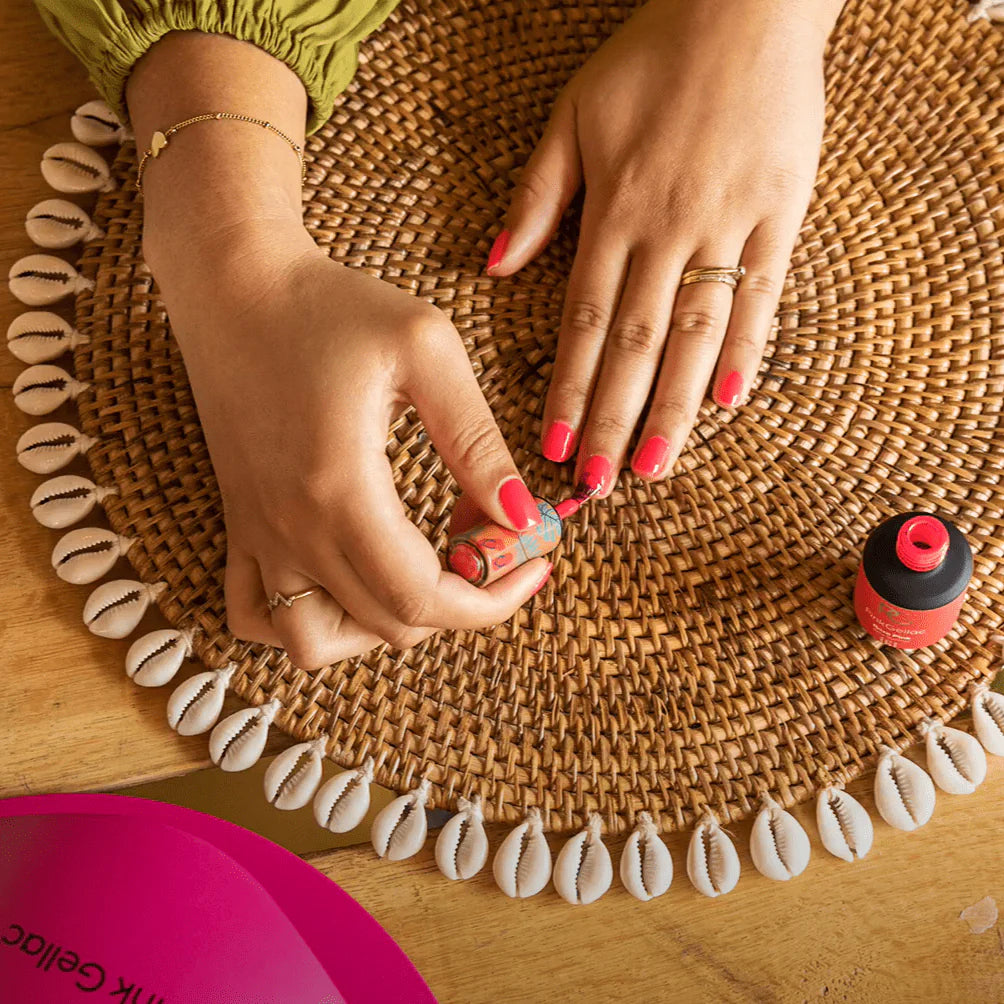 Hand with pink nail polish, wicker placemat with shells.