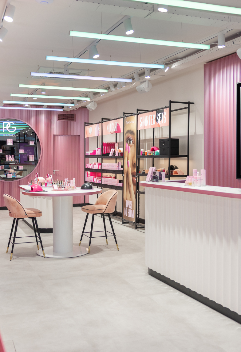 Pink decorated nail studio with tables, products and promotional material, including neon lighting and modern furniture.