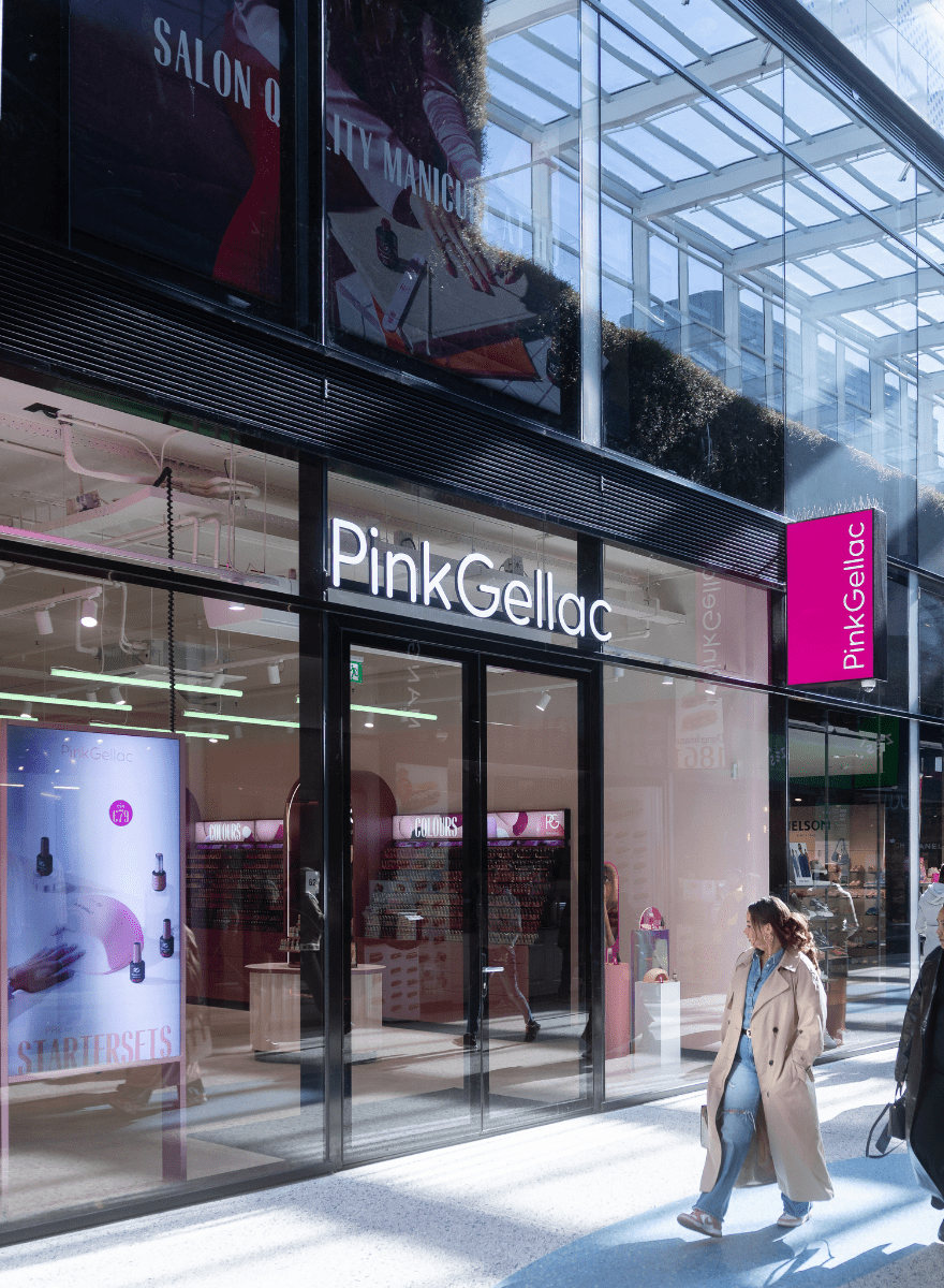 PinkGellac storefront with glass doors and a woman walking by in a shopping mall.