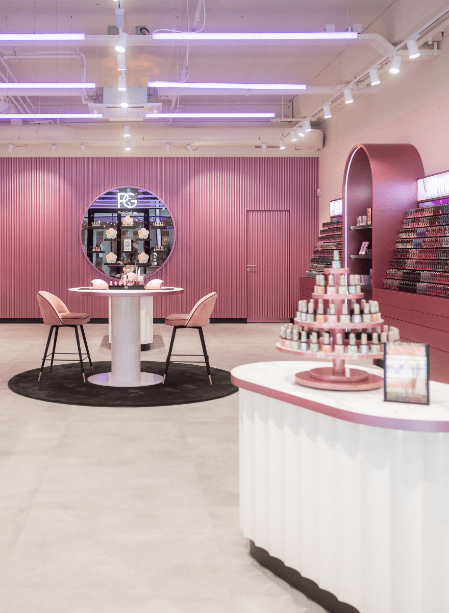A modern and stylish nail salon with pink and purple accents, decorated with sleek furniture, a table with chairs and a display with nail polish bottles.