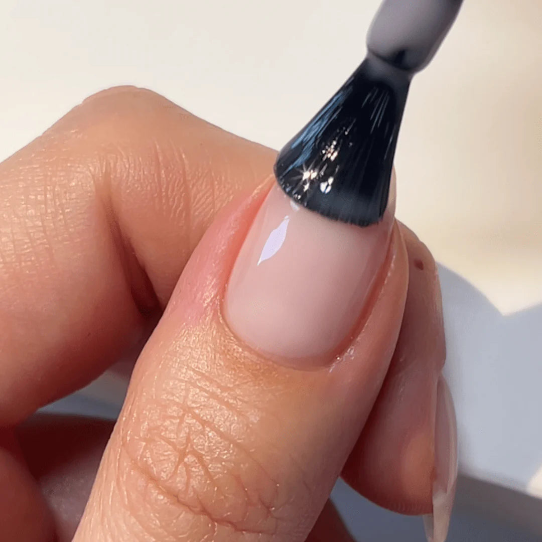 A close-up of a hand applying nail polish to a nail with a brush.