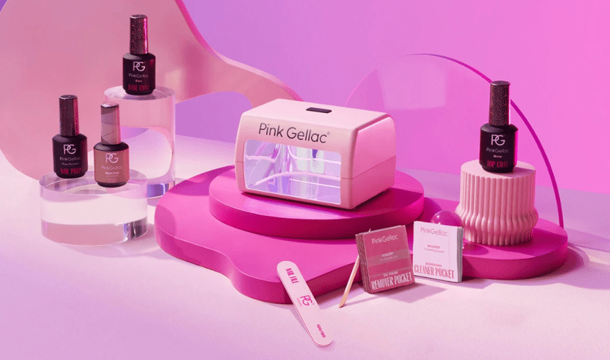 Pink nail products on display with Pink Gellac LED lamp, nail polishes, file and cleaning wipes, against a pink background.