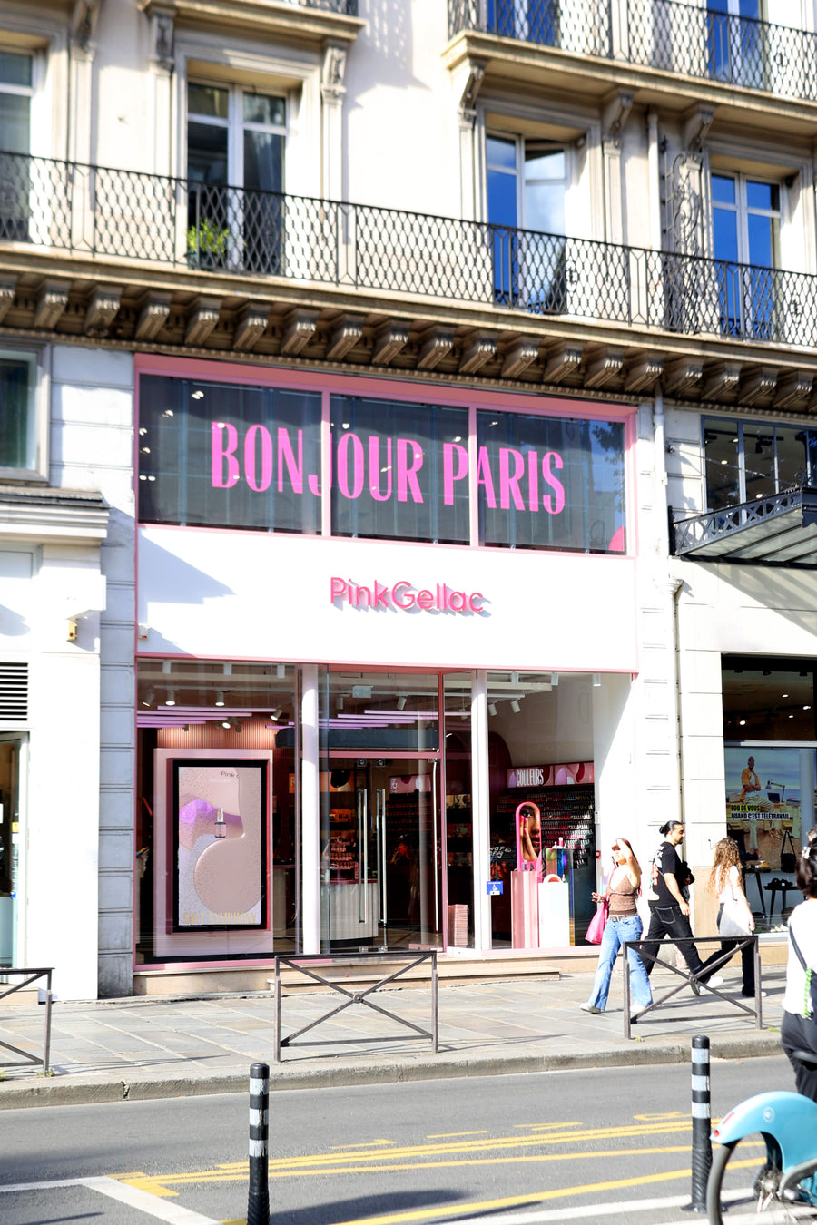 Exterior view of a shop with the text "Bonjour Paris" and "PinkGellac" on the façade, with passers-by on the pavement.
