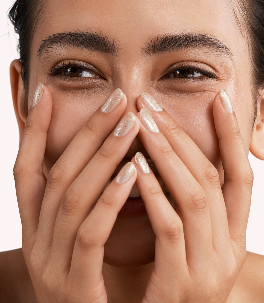 Close-up of a woman with Pink Gellac 174 Diva Gold manicured nails near her face.