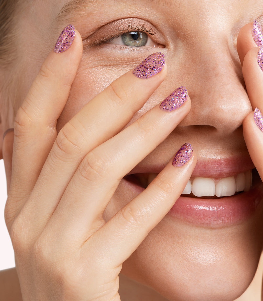 Close-up of a woman with Pink Gellac 206 Bedazzled Purple manicured nails near her face.