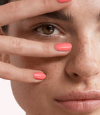 Close-up of a woman with Pink Gellac 240 Salmon manicured nails near her face.