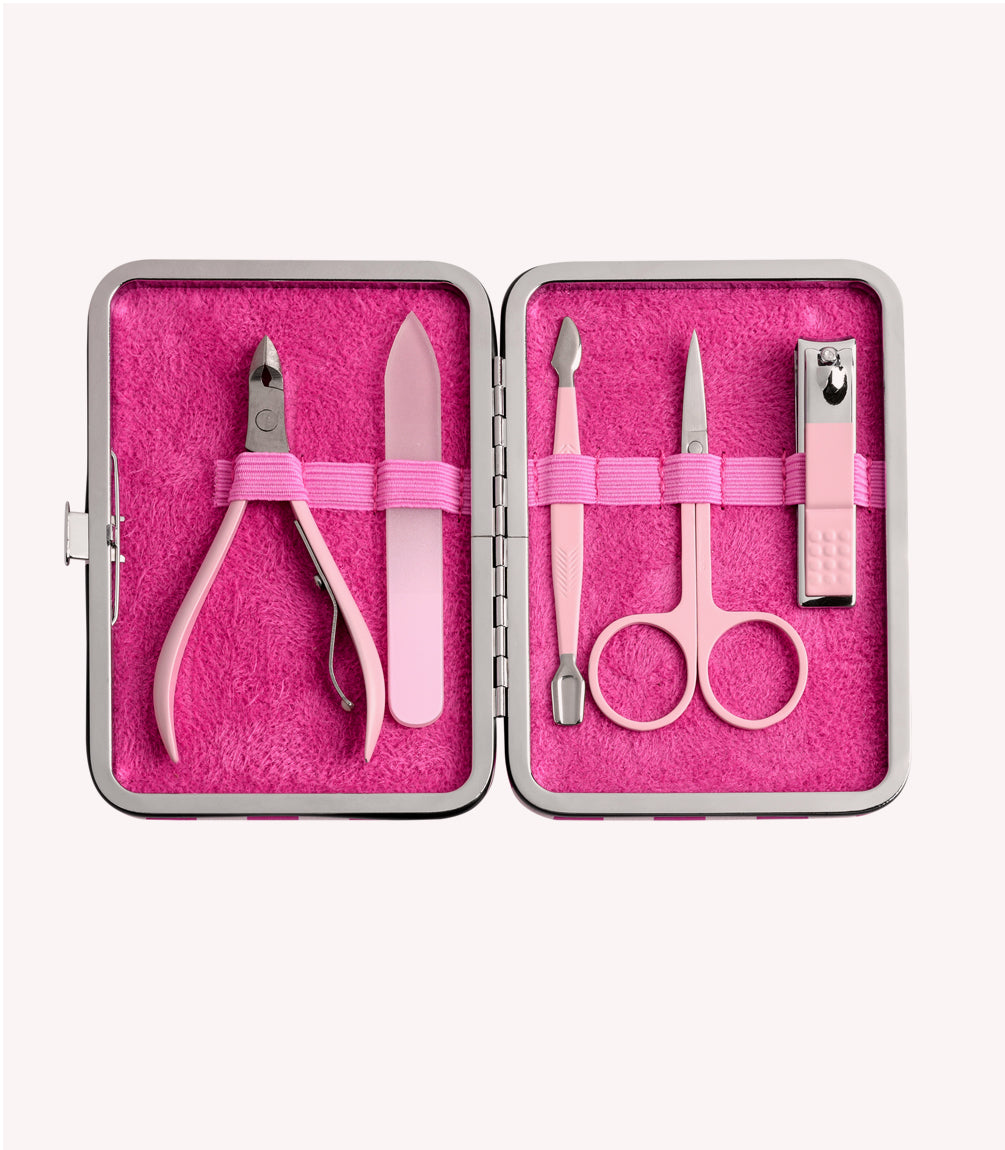 Pink manicure set in an open metal box with nail scissors, nail clippers, file and flash on a pink velvet background.