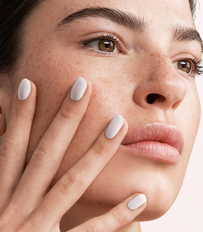 Close-up of a woman with Pink Gellac 101 Soft White manicured nails resting against her face.