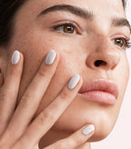 Close-up of a woman with Pink Gellac 101 Soft White manicured nails resting against her face.