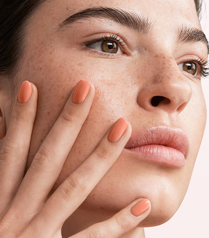 Close-up of a woman with Pink Gellac 106 Nude Orange manicured nails near her face.