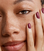 Close-up of a woman with Pink Gellac 111 Rustic Red manicured nails near her face.