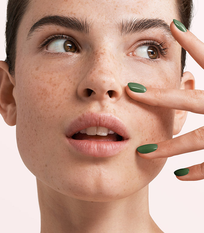 Close-up of a woman with Pink Gellac 261 Forest Green manicured nails near her face.