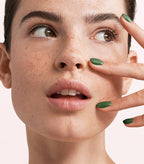 Close-up of a woman with Pink Gellac 261 Forest Green manicured nails near her face.