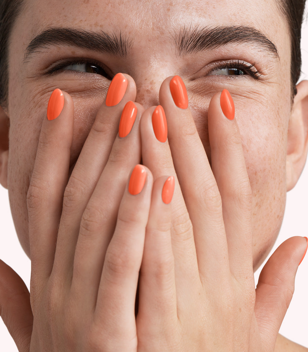 Close-up of a woman with Pink Gellac 327 Mandarin Orange manicured nails near her face.