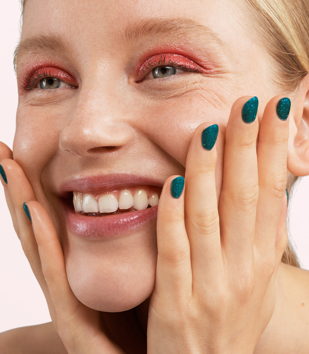Close-up of a woman with Pink Gellac 429 Twinkling Emerald manicured nails near her face.