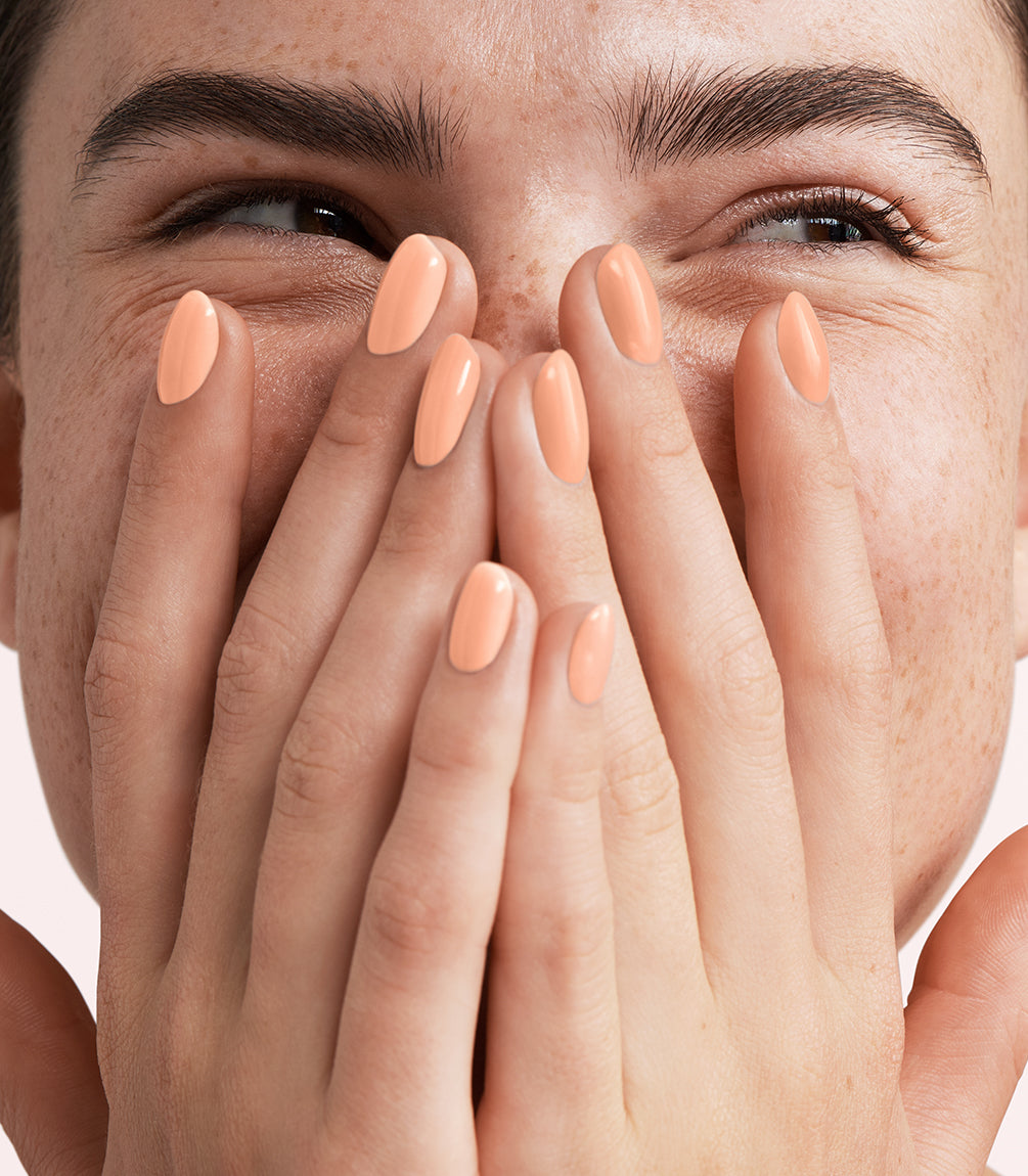 Close-up of a woman with Pink Gellac 446 Blushing Peach manicured nails near her face.