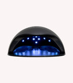 Black UV/LED nail lamp with blue lights inside, used for curing gel nail polish.
