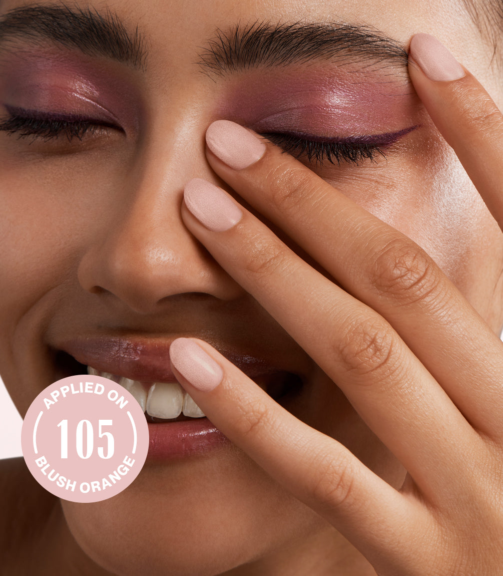 Smiling person with pink eyeshadow and light nail polish holds her hand in front of the face, with the text "Applied on 105 Blush Orange" on the image.