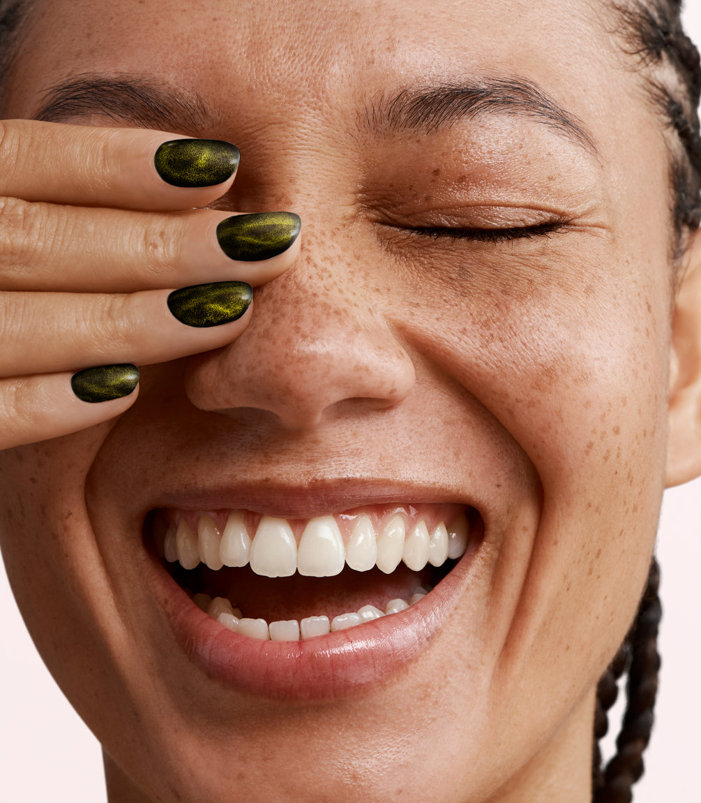Close-up of a woman with Pink Gellac Cat Eye Sunstone Gold manicured nails near her face.