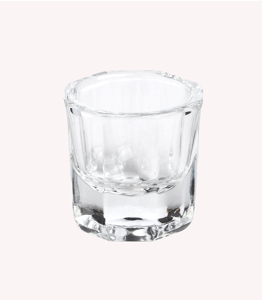 An empty, transparent shot glass against a neutral, light background.
