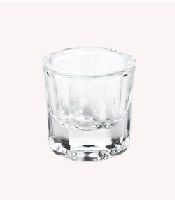An empty, transparent shot glass against a neutral, light background.