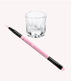 Pink manicure brush with black tips and a small, clear glass jar on a light background.