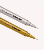 Two permanent markers, one silver and one gold, with a fine tip of 1.8 mm, lying on a light background.