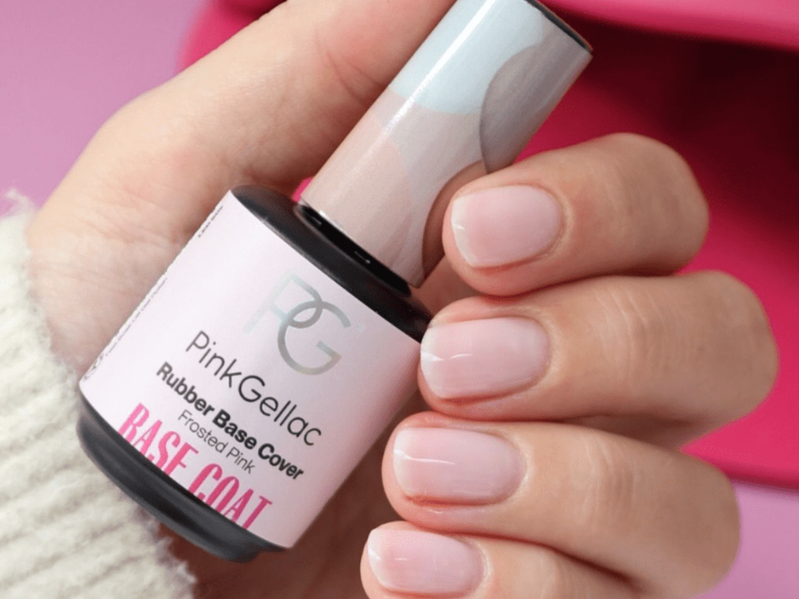A hand with well-groomed nails holds a bottle of Pink Gellac Rubber Base Cover in Frosted Pink.