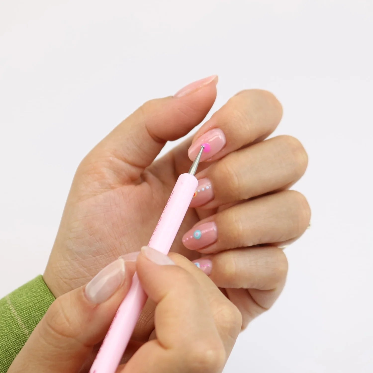 Two hands busy applying pink dots on nails with a nail art pen.