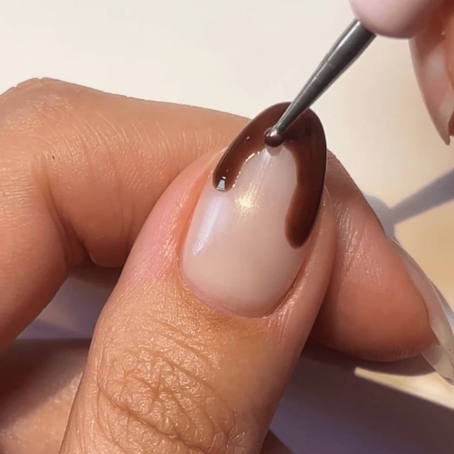 A hand applying nail polish in brown shade to the nail with a brush.